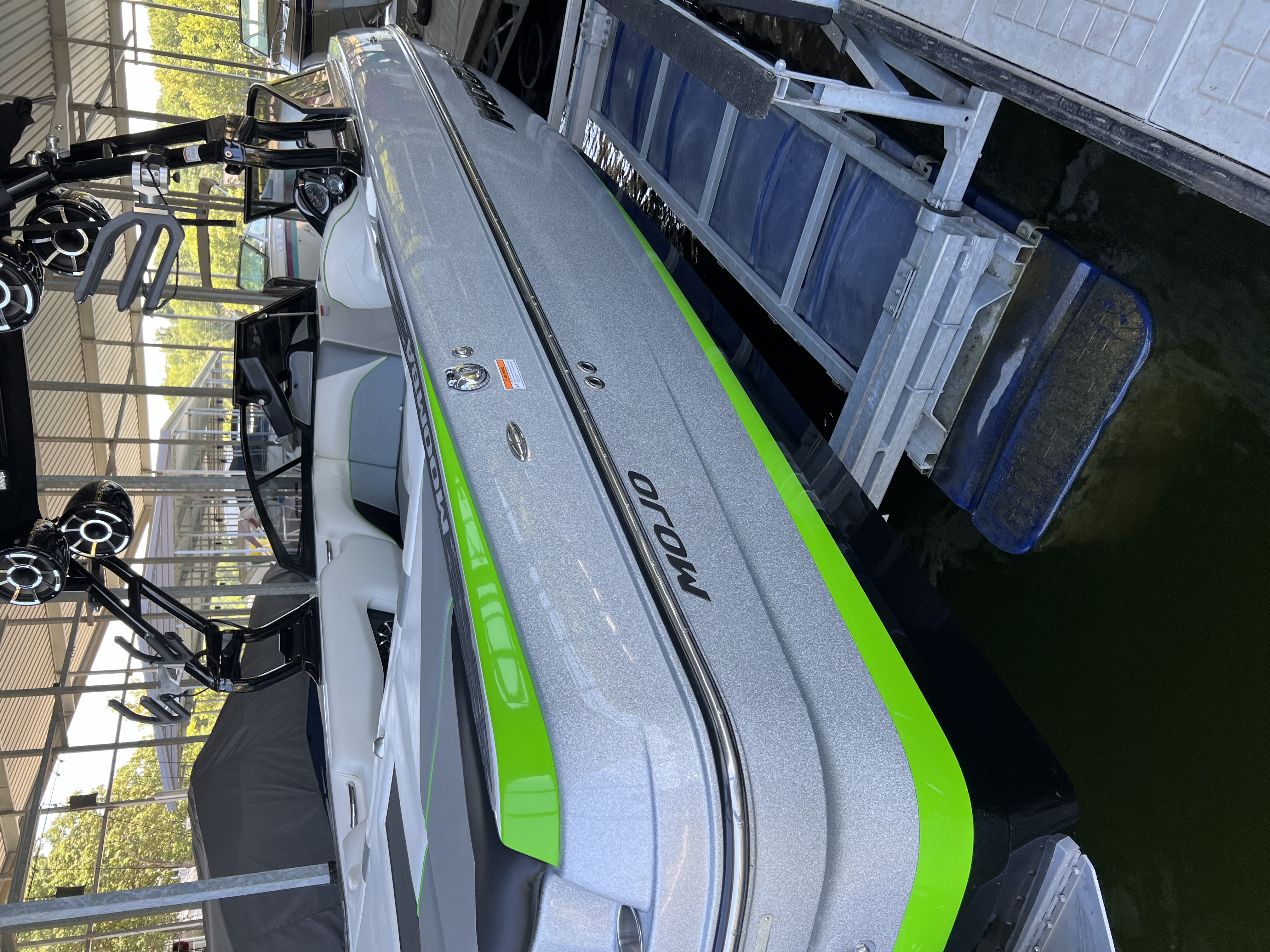 Silver and lime green Moomba Mojo wake boat on a lift under a covered dock