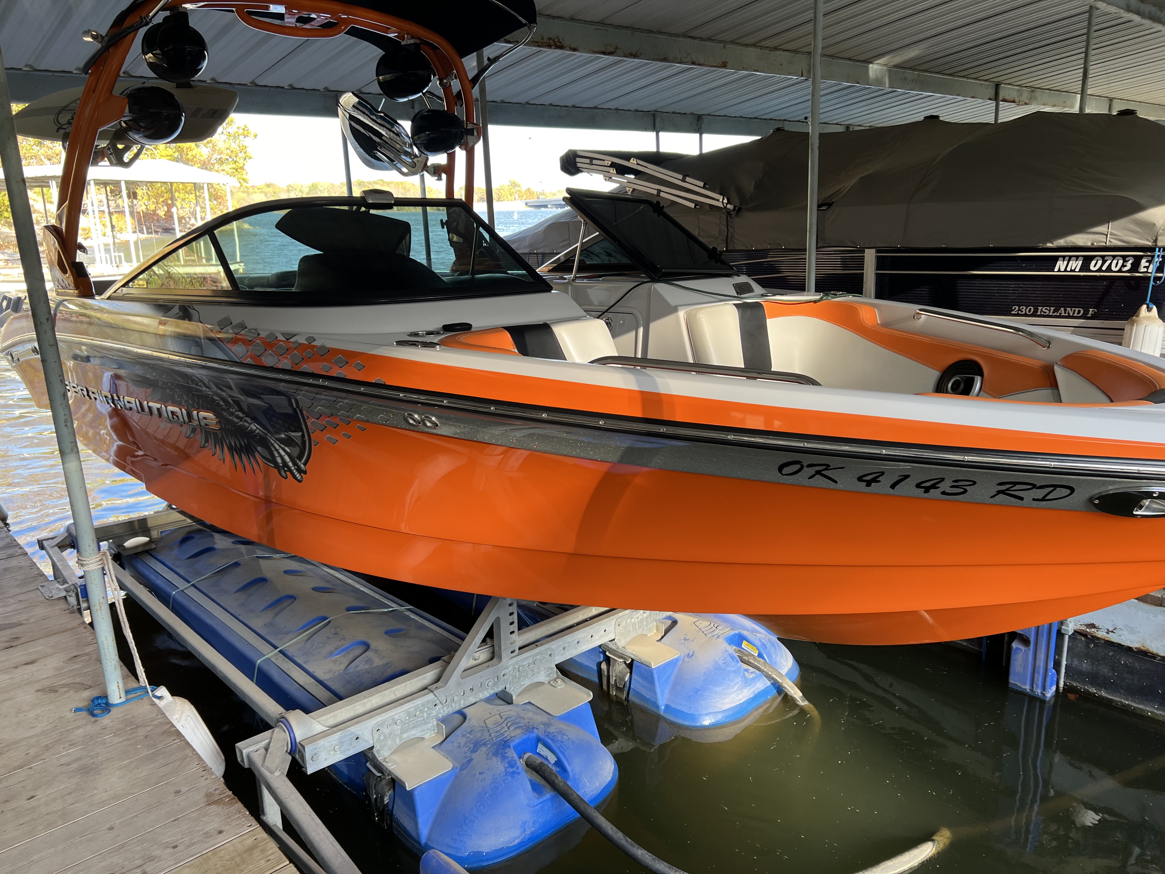 Polished orange, white and black Super Air Nautique wake boat on a lift under a covered dock